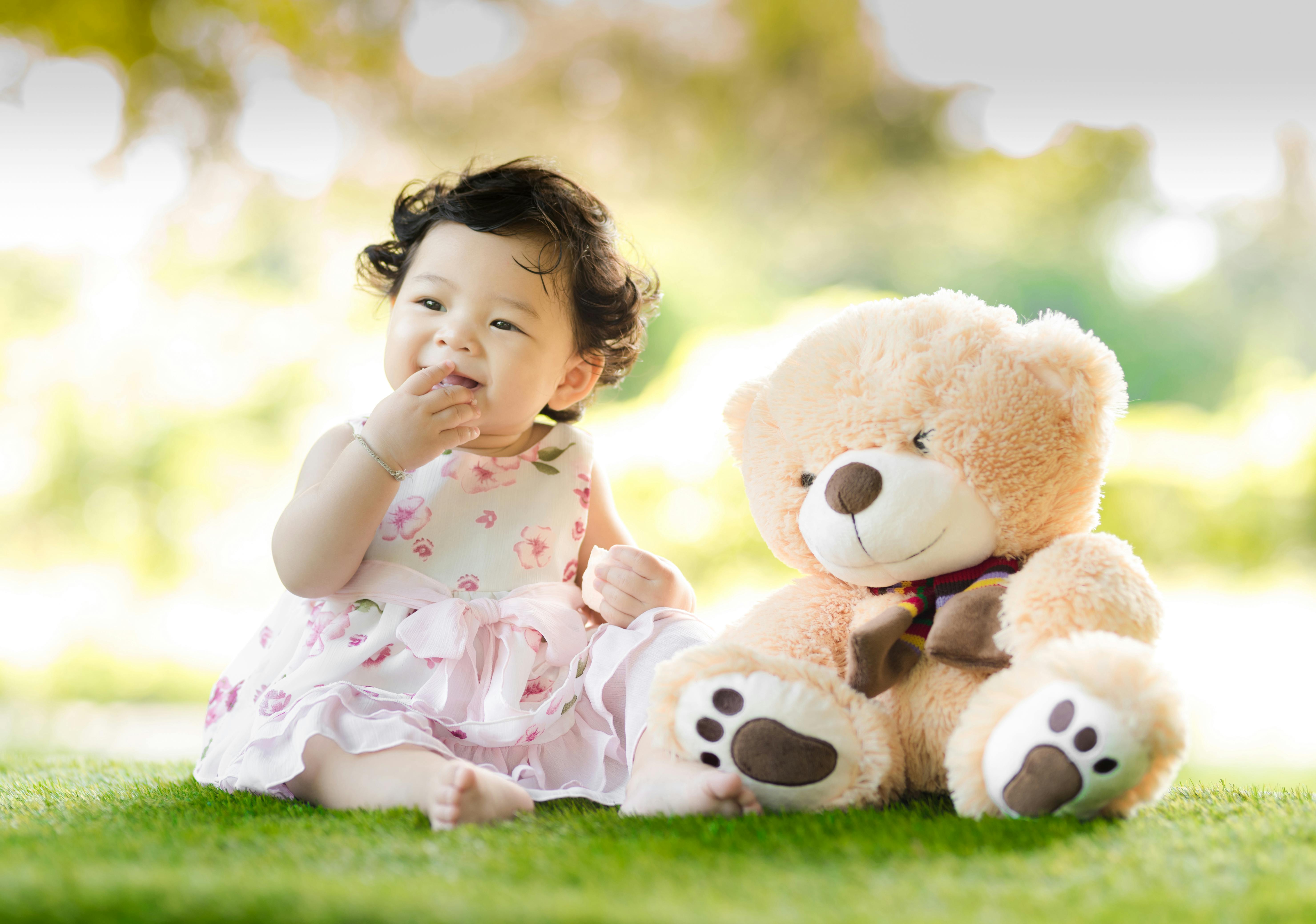 Baby sitting on the grass with a big teddy bear